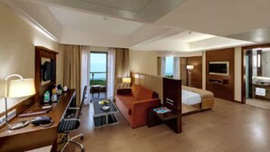 A hotel room with a desk, a sofa, a bed, a TV, and a view of the outdoors. - The Fern Kadamba Hotel & Spa Goa, Panjim, Series by Marriott (Panaji)