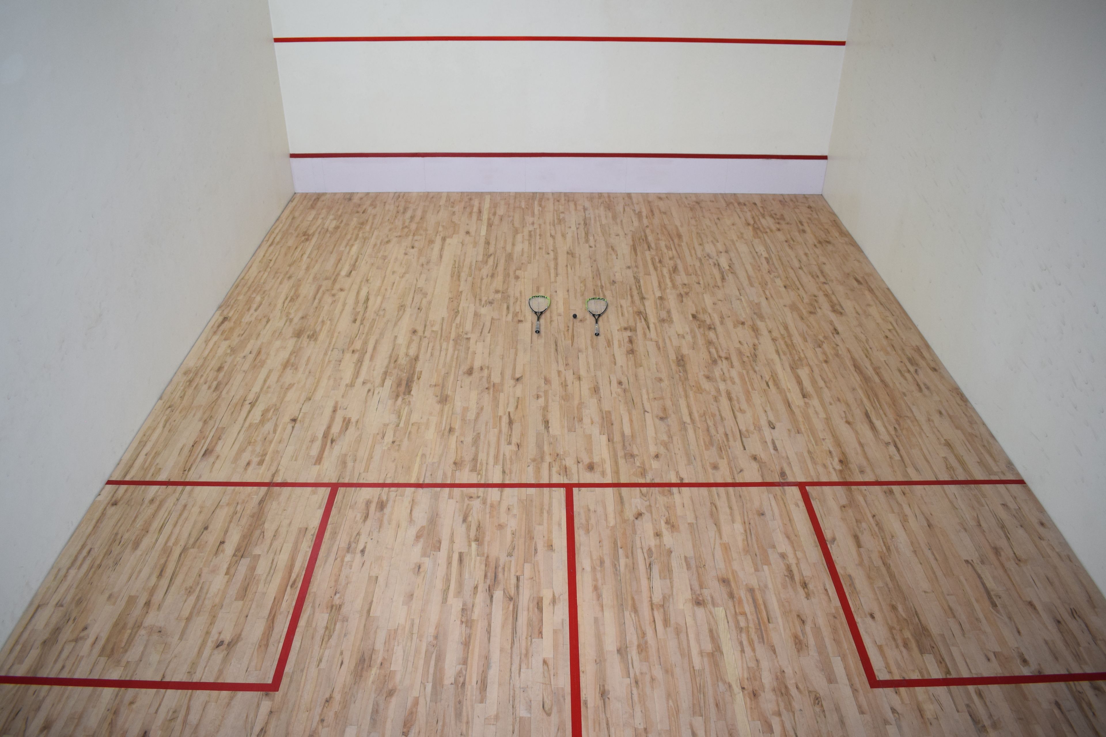 A squash court with a wooden floor and red lines marking the boundaries.