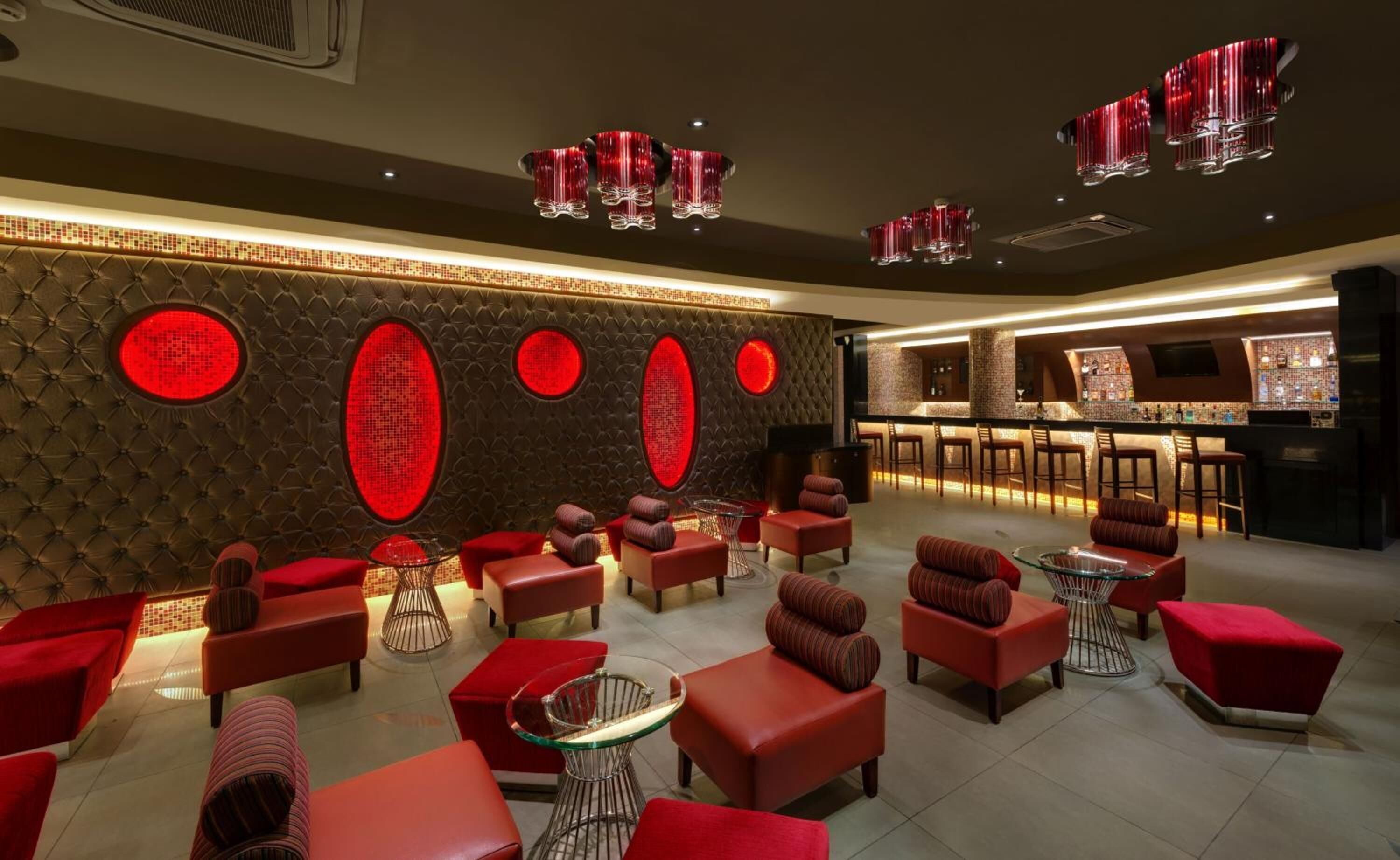 A modern lounge area with red upholstered seating, a bar, and decorative red lighting.