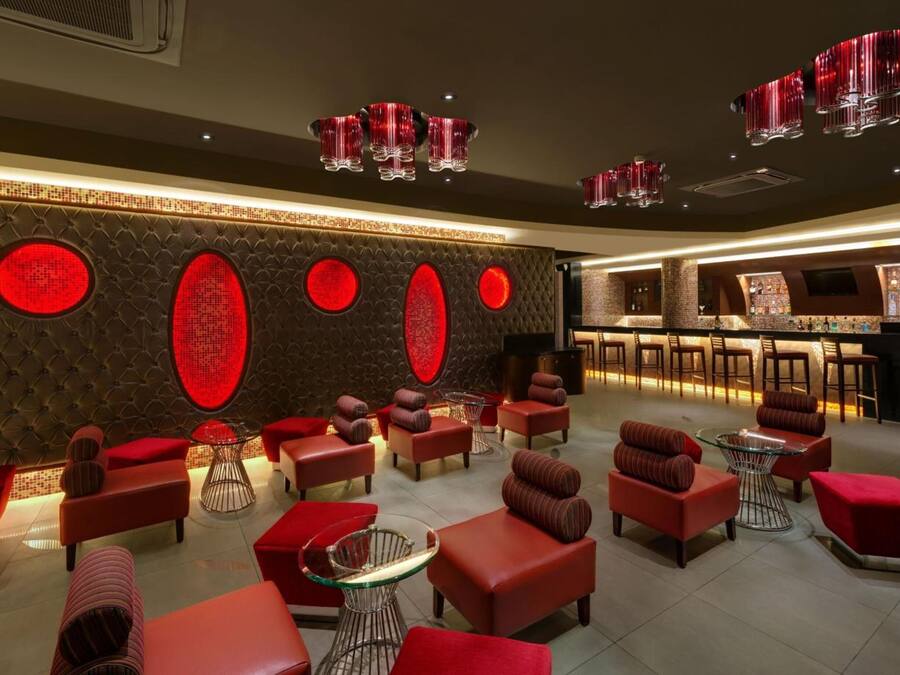 A modern lounge area with red upholstered seating, a bar, and decorative red lighting.