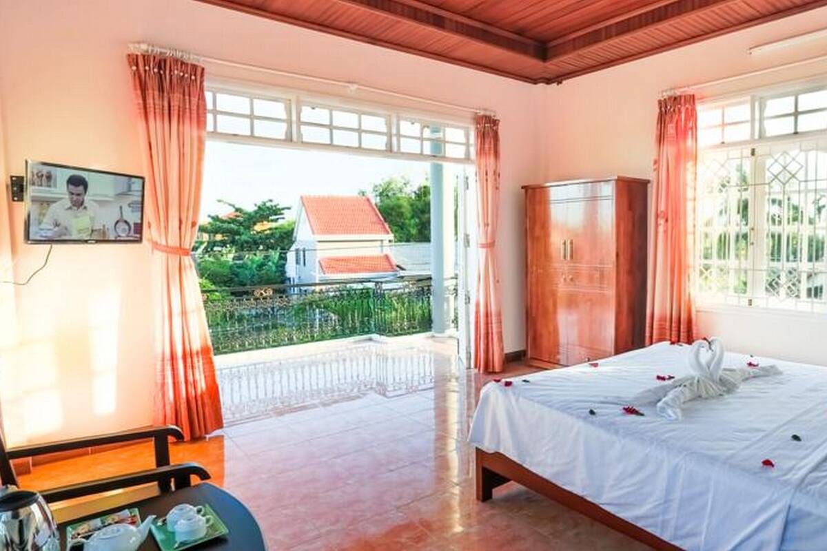 Habitación de hotel con cama, escritorio y armario. Cuenta con ventanas con cortinas y vistas a una casa.