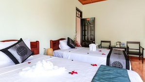 A hotel room with two beds, each with a pillow featuring a geometric design. There is a small table with a kettle and a chair. - Rice Village Homestay (Da Nang)