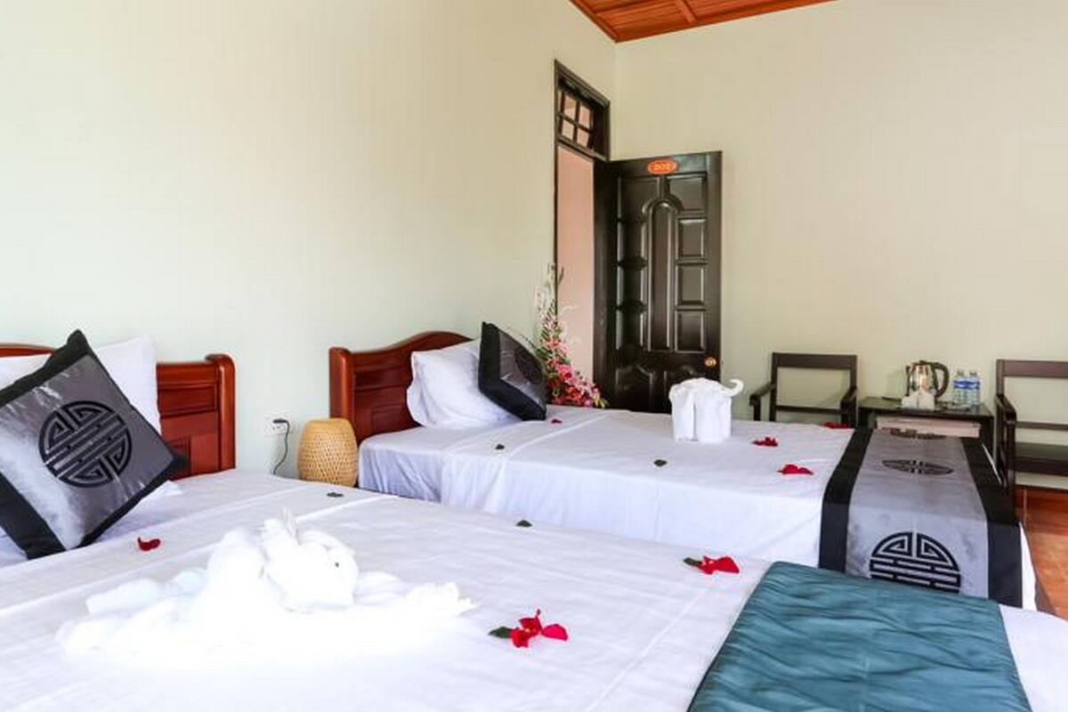 Habitación de hotel con dos camas, cada una con un almohadón de diseño geométrico. Hay una mesita con una tetera y una silla.
