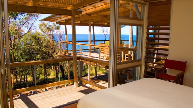 Un dormitorio con un ventanal grande que da a una terraza y al mar.