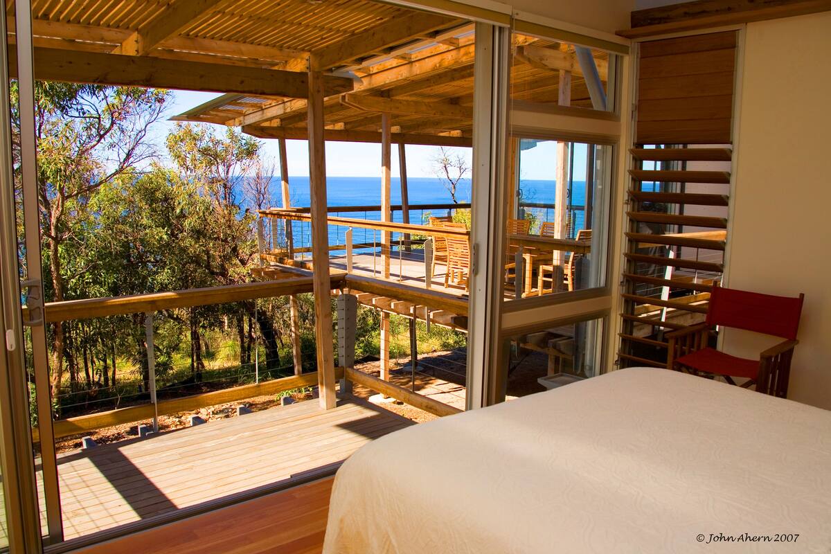Ein Schlafzimmer mit großem Fenster mit Blick auf eine Terrasse und das Meer.