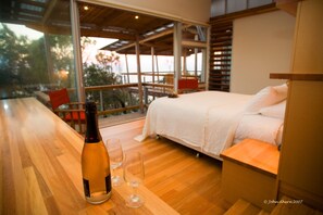 Ein modernes Schlafzimmer mit einem großen Bett, Holzboden und einem Balkon mit Blick.