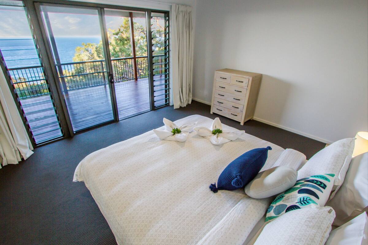 Ein Hotelzimmer mit einem großen Bett, einem Schminktisch und einem Balkon mit Meerblick.