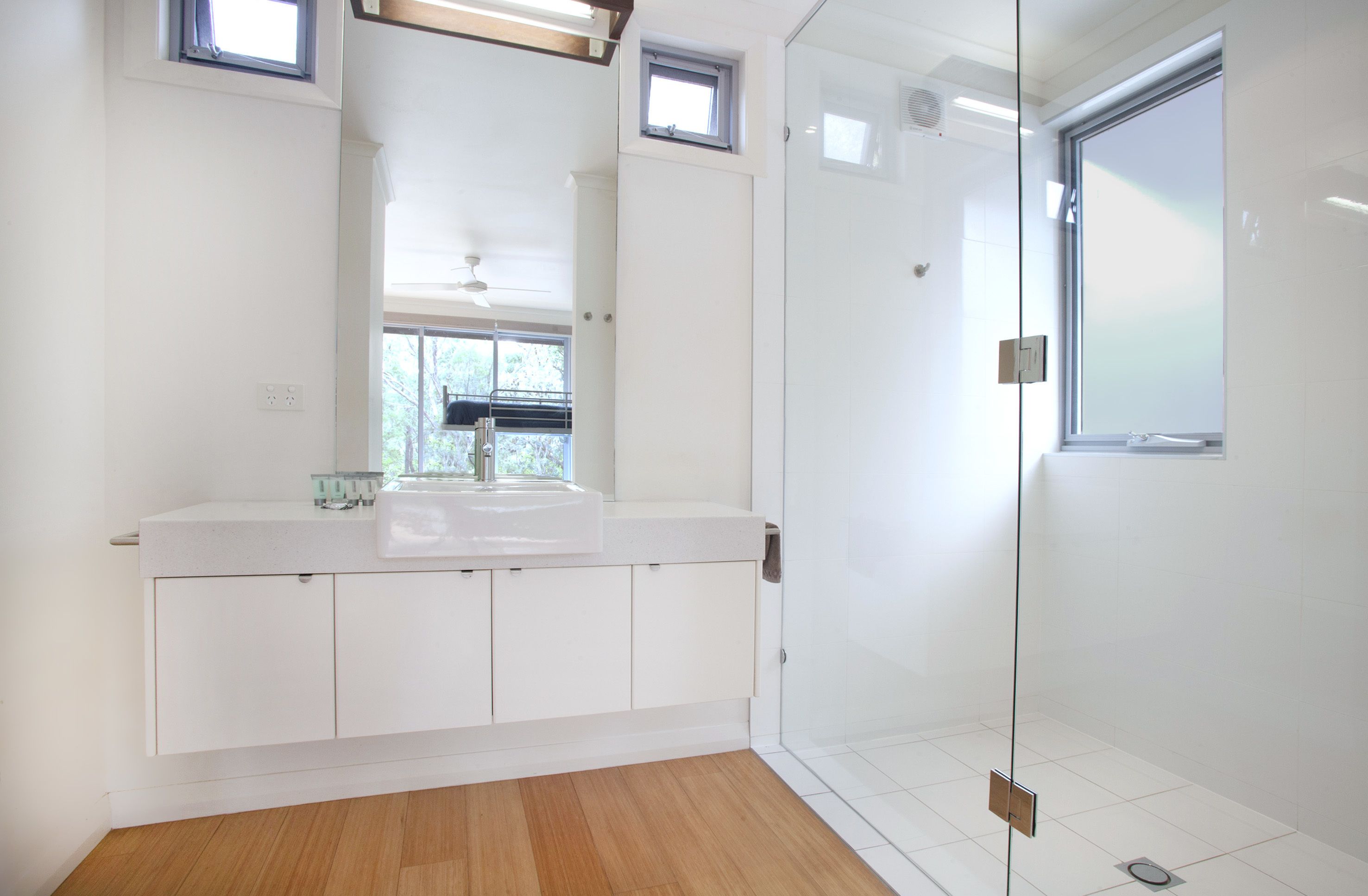 Une salle de bain moderne dotée d’une douche à parois de verre, d’un meuble-lavabo blanc et d’une fenêtre laissant entrer la lumière naturelle.