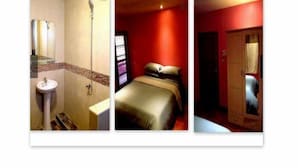 Une salle de bain avec un lavabo et une douche, un lit avec un mur rouge et une fenêtre, et une armoire en bois.
