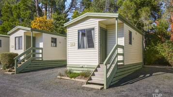 A row of small, single-story mobile homes with green trim, each featuring a front porch and a staircase leading to the entrance.
