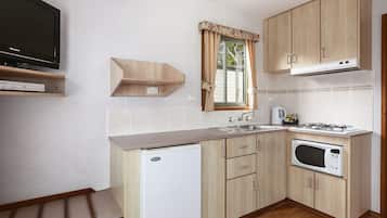 A compact kitchen with a built-in microwave, a gas stove, a sink, and a television on a shelf.