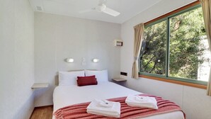 Habitación de hotel con una cama grande, ventilador de techo, ventana con cortinas y mesita de noche con lámpara.