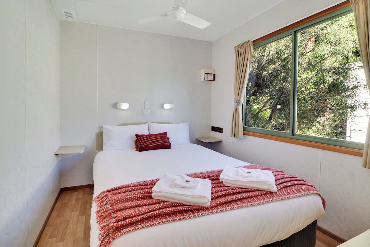 A hotel room with a large bed, a ceiling fan, a window with curtains, and a bedside table with a lamp.