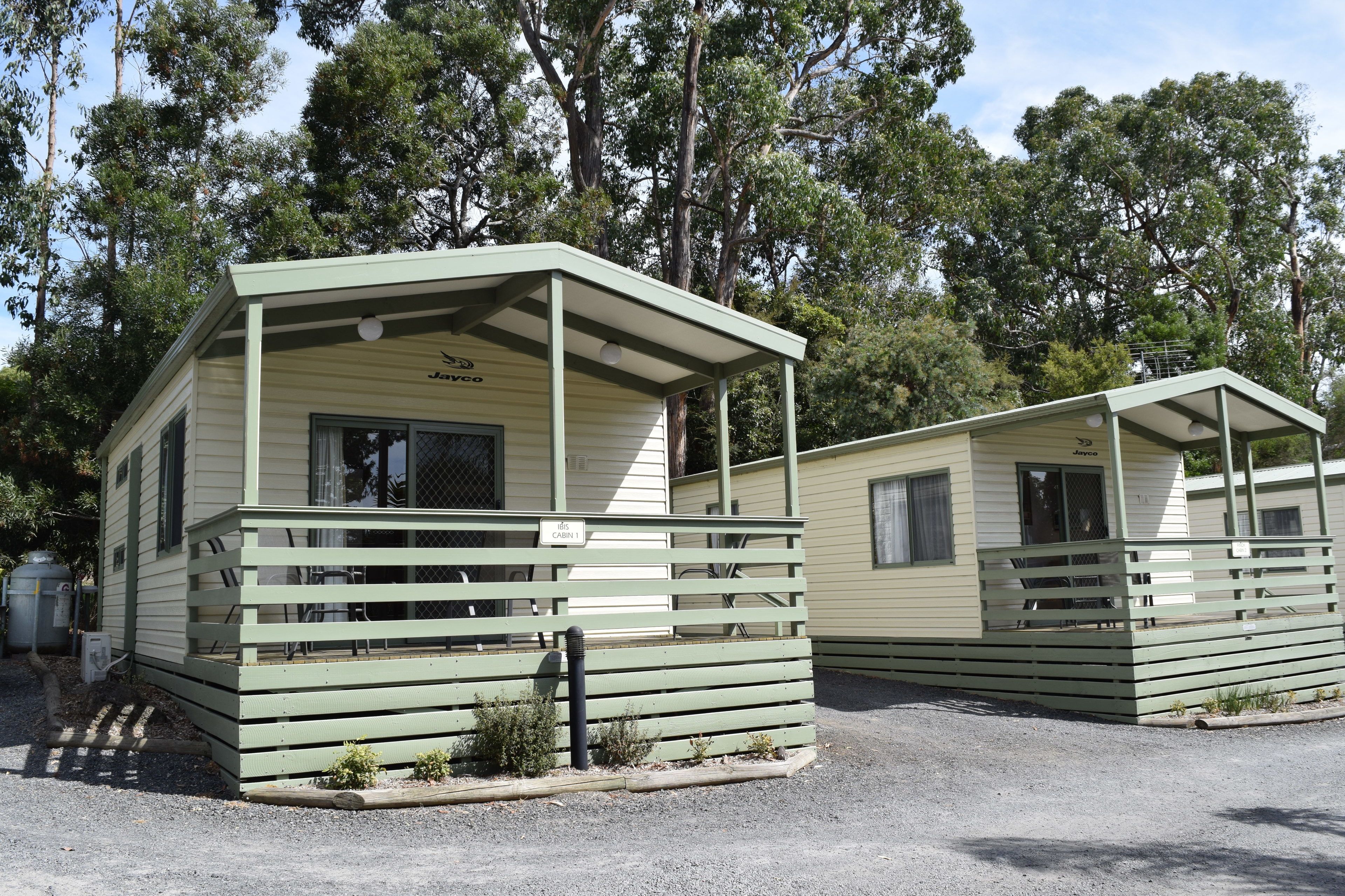 Two cabins with a porch, a small garden area, and a gravel driveway.