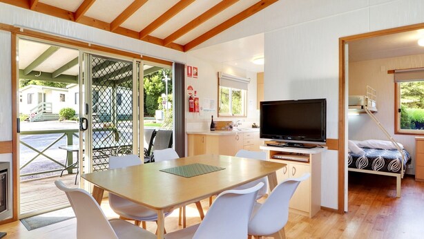 Una habitación acogedora con una mesa de comedor de madera, sillas blancas, un televisor y una cama litera.