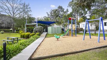 Explore the playground area surrounded by lush landscaping and a wooden pathway leading to a picnic table.