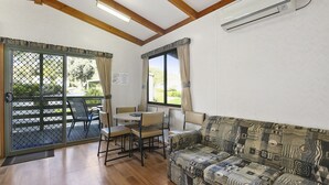 Una habitación con piso de madera, un sofá estampado, una mesa con sillas y una puerta corrediza de vidrio que da a un área exterior con patio y sillas.