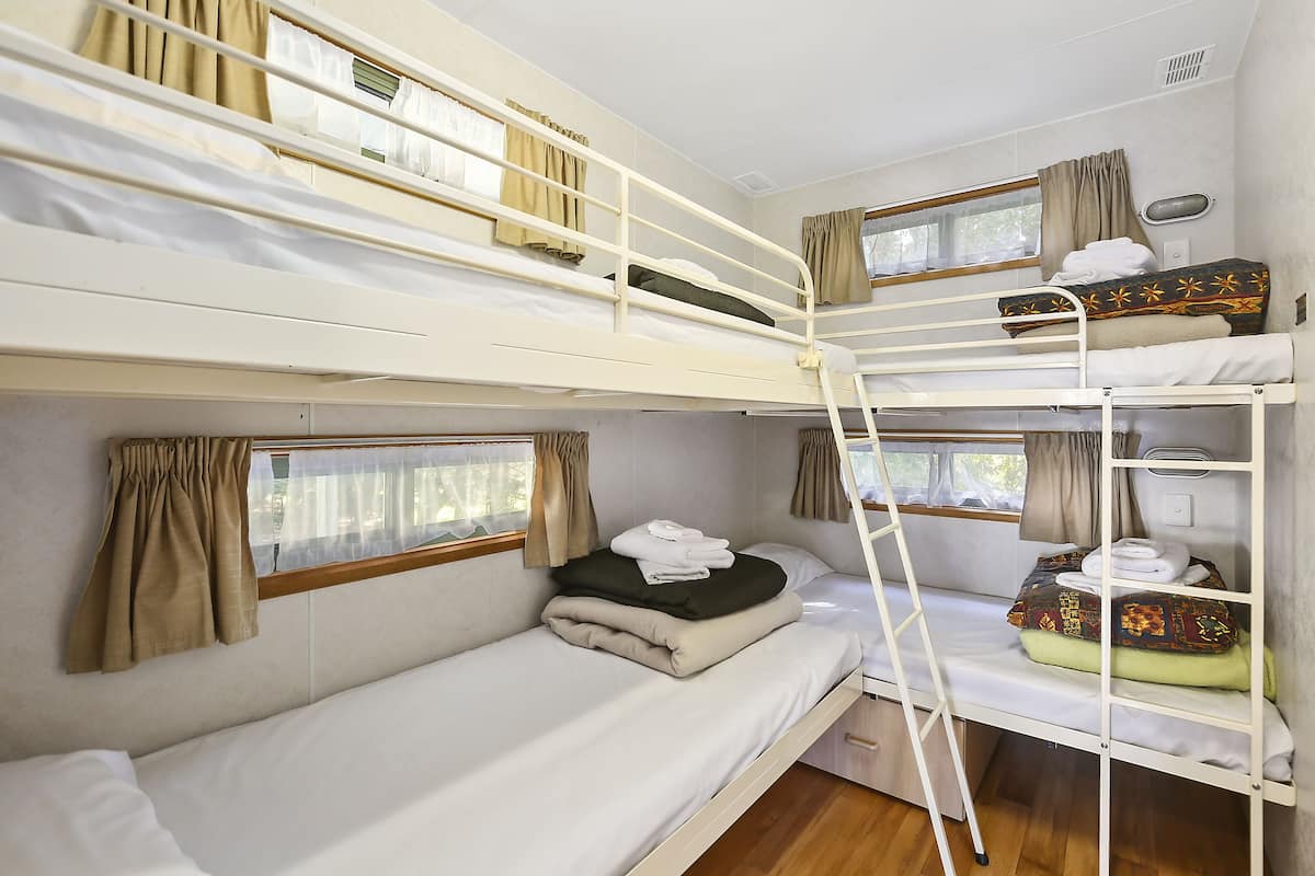 A bunk bed room with a ladder, curtains, and a window.