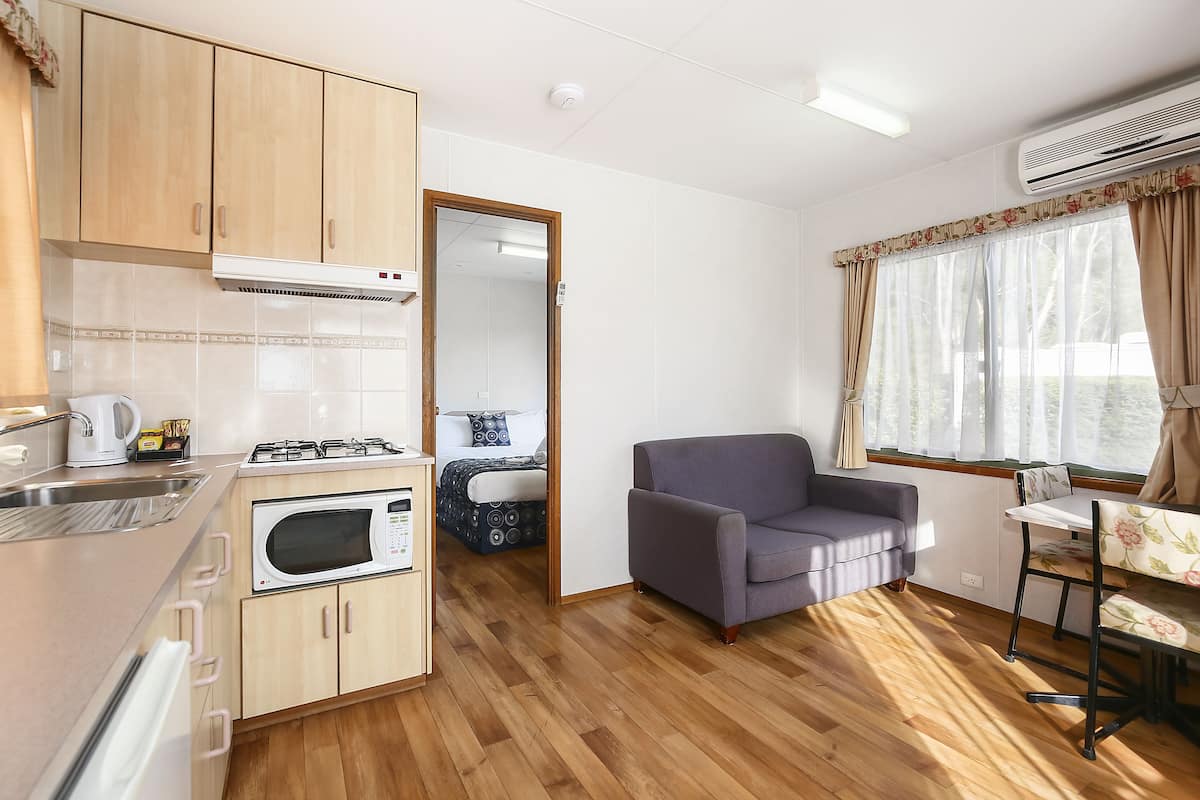 A compact living space with a kitchenette, a sofa, a dining table, and a window with curtains.