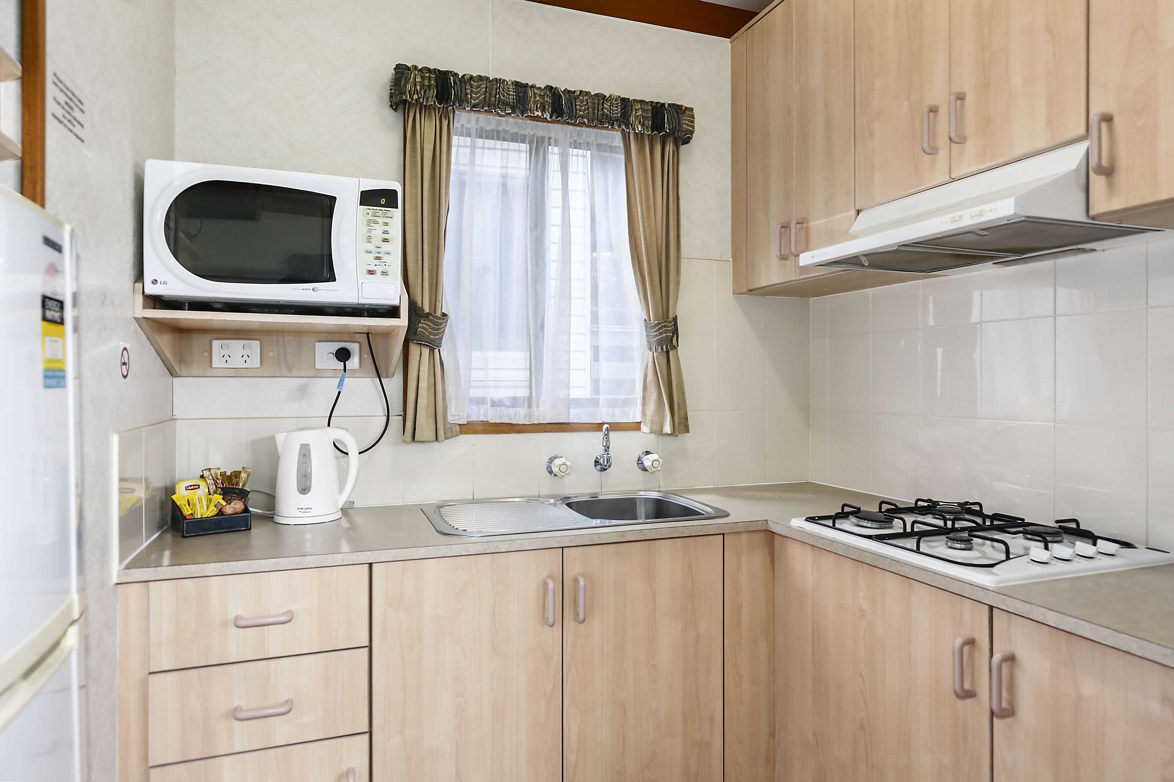 A compact kitchen with a microwave, kettle, sink, and gas stove.
