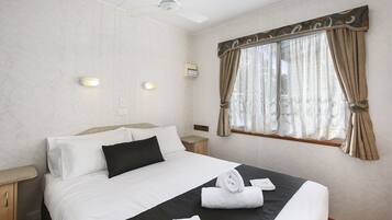 Una cama bien hecha con ropa de cama blanca y negra, un ventilador de techo y una ventana con cortinas.