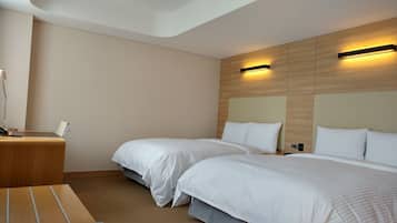 Habitación de hotel con dos camas, un escritorio con lámpara y cabecera de madera con iluminación integrada.