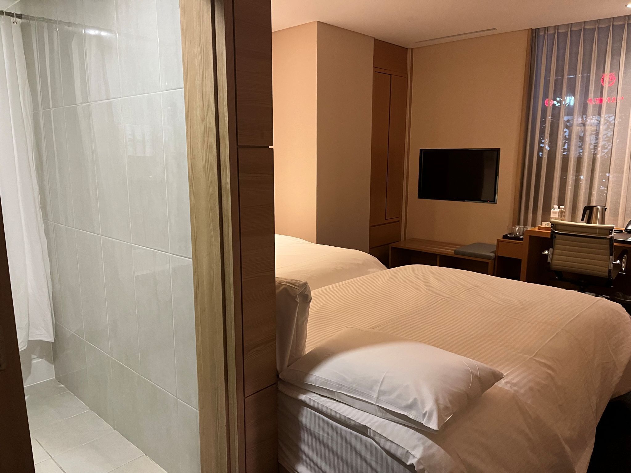 Habitación de hotel con una cama grande, un televisor montado en la pared, un escritorio con una silla y zona de ducha.
