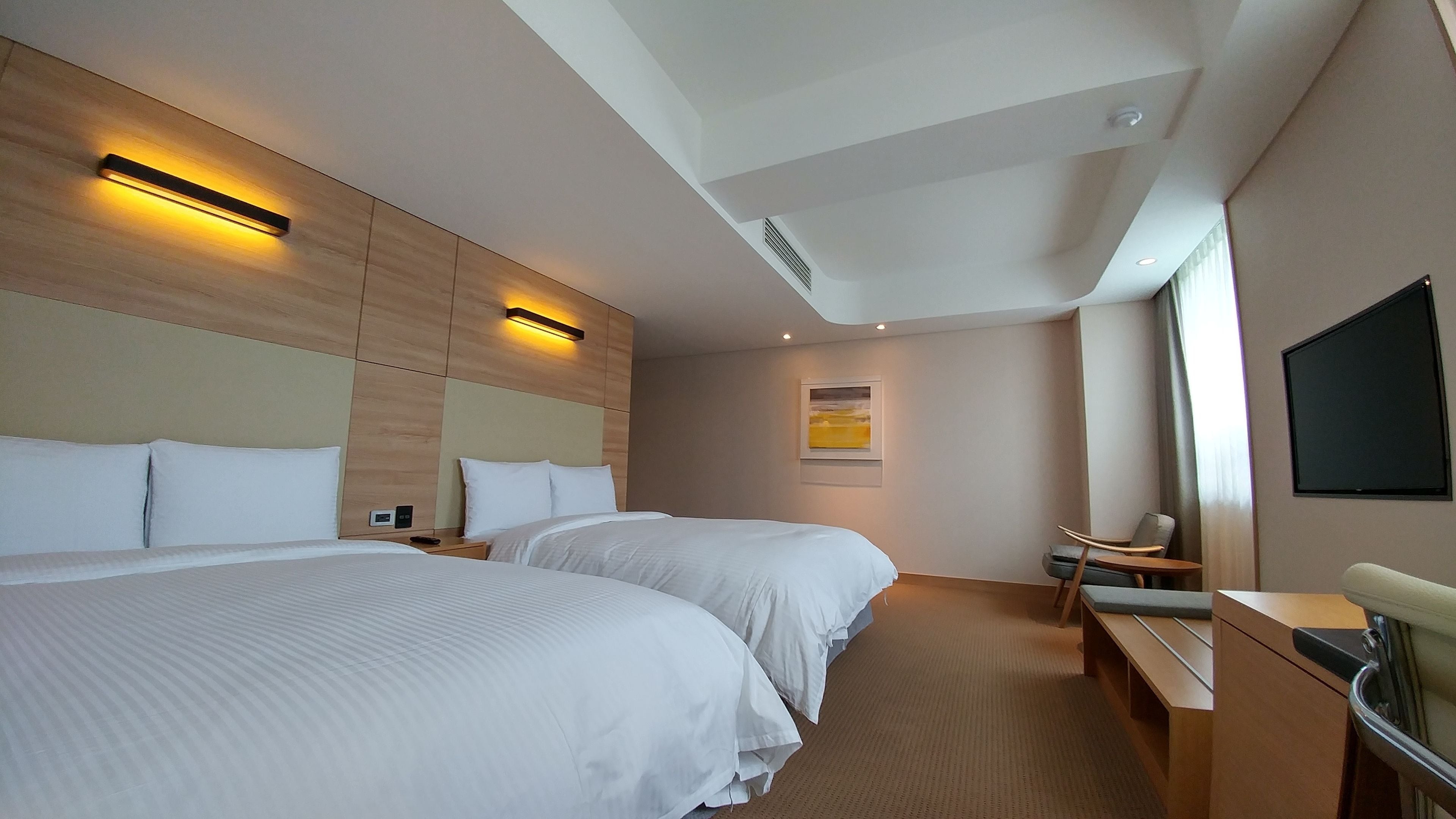 A hotel room with two beds, a desk, a chair, a TV, and a painting on the wall.