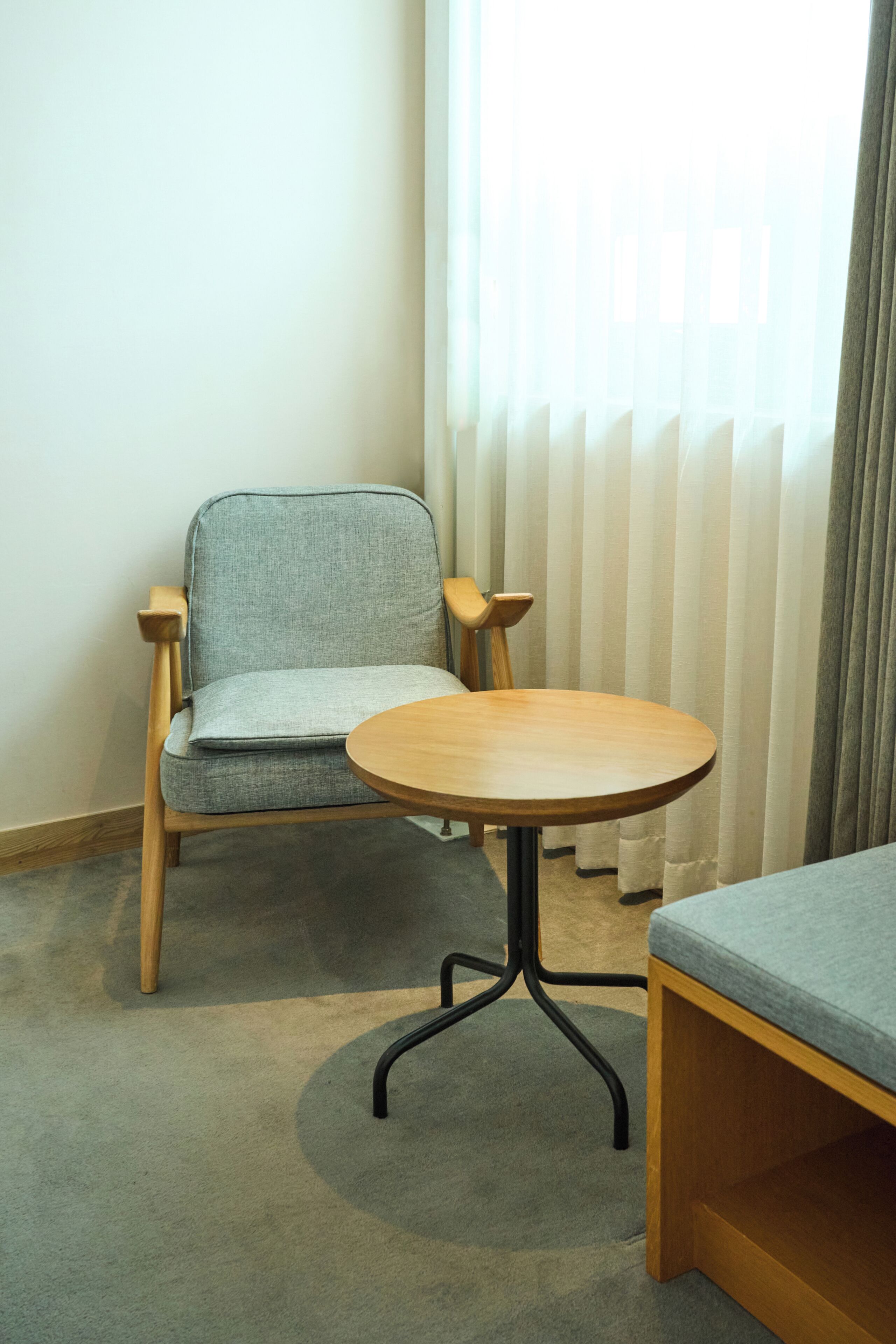 Una habitación con una silla de madera, una mesa redonda y una ventana con cortinas.