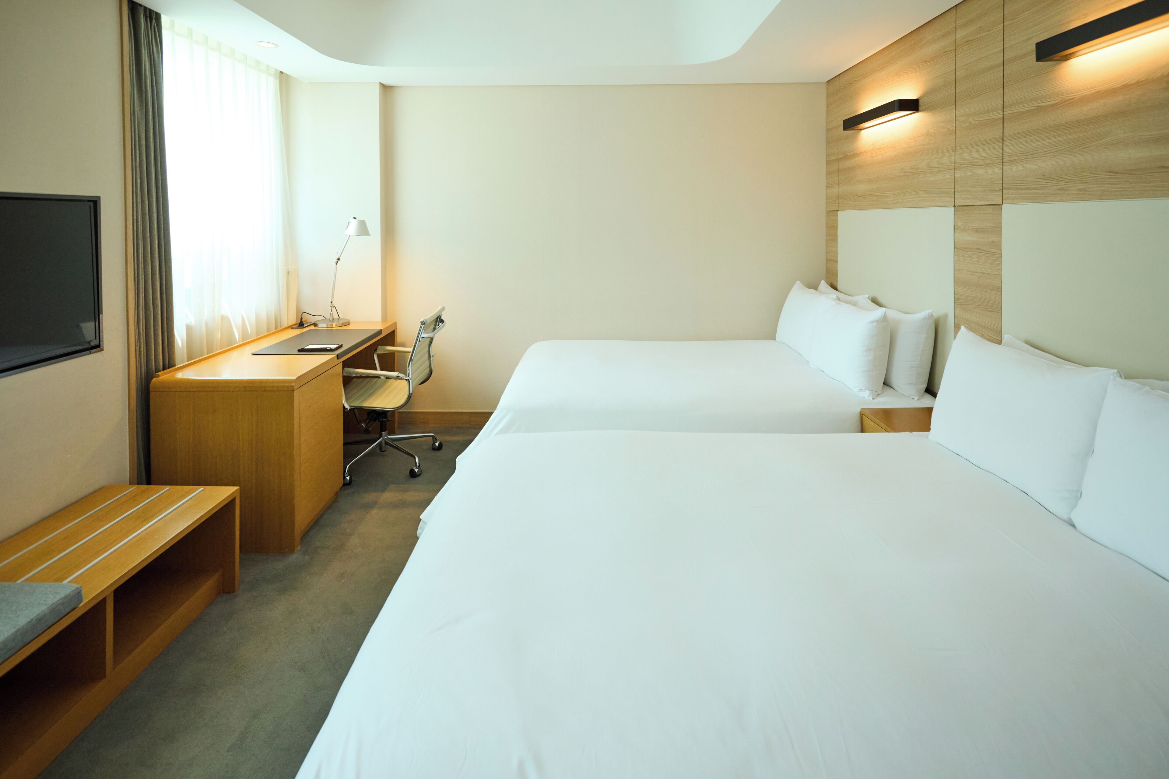 Hotellihuone, jossa on kaksi sänkyä, työpöytä, tuoli, televisio ja ikkuna, jossa on verhot.