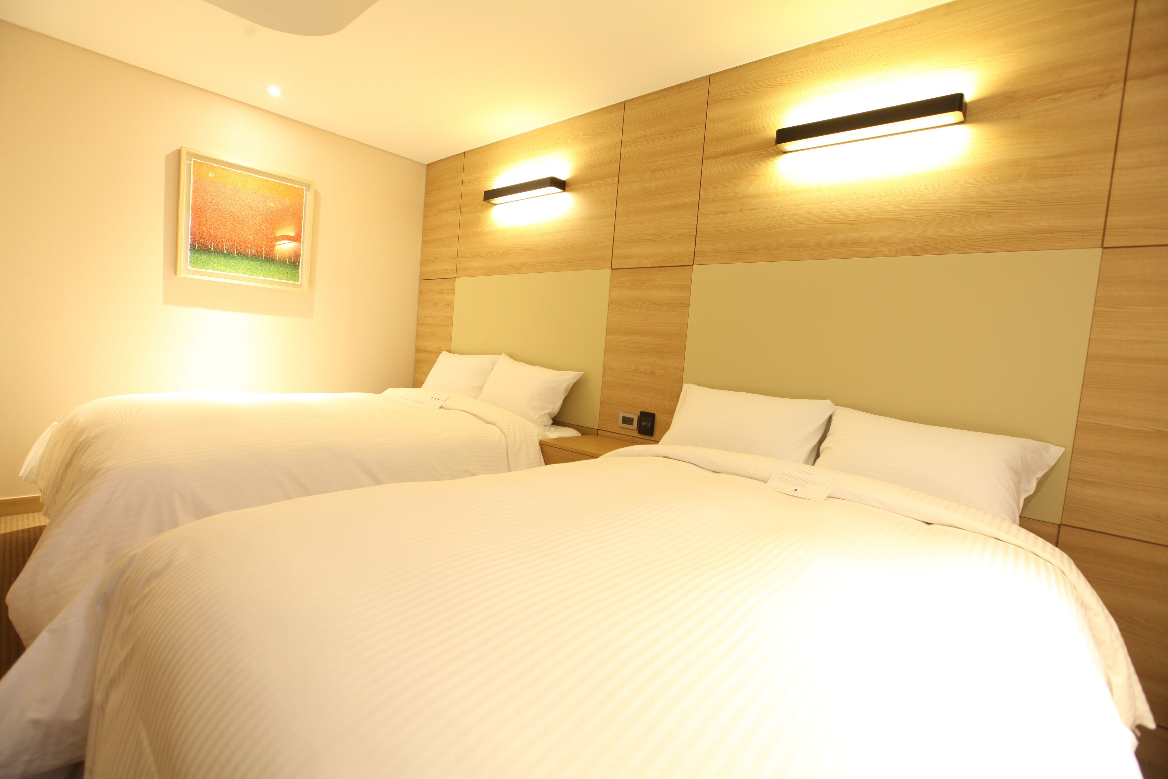 A hotel room with two beds, wooden headboards, and wall-mounted lighting.