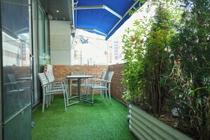 A patio area with a table and chairs, a brick wall, and a blue canopy. - Acube Hotel (Seoul)