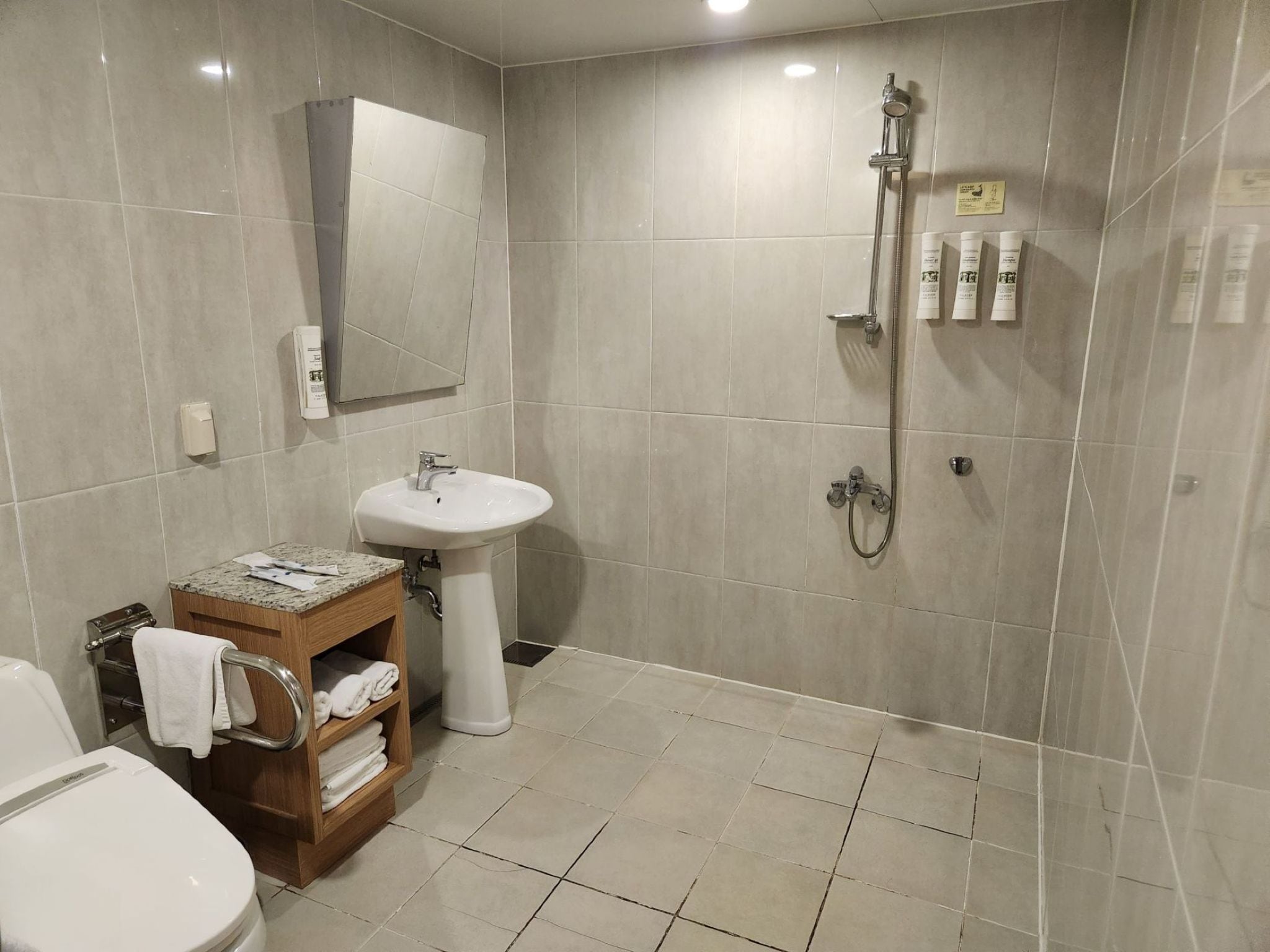 Un baño con inodoro, lavamanos, ducha y un estante de madera con toallas.