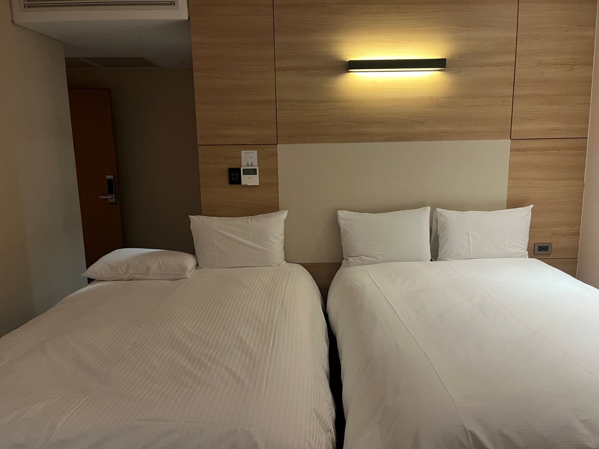 Habitación de hotel con dos camas, cabecera de madera y lámpara fijada a la pared.