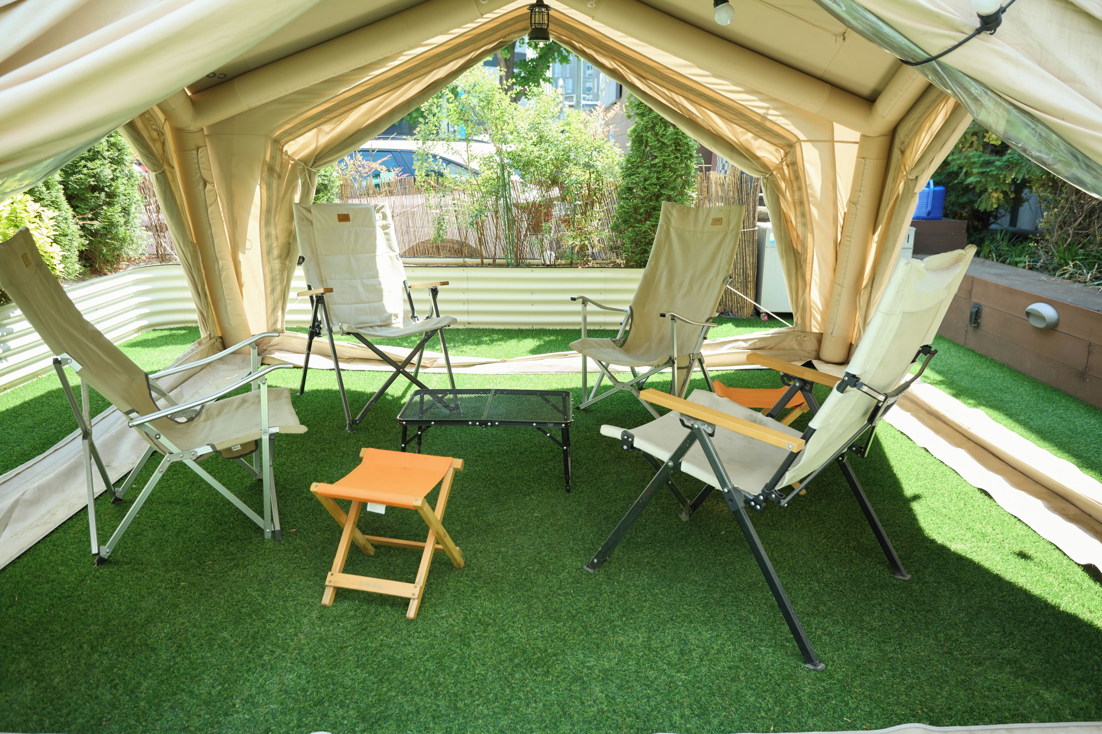 Een tent met vier canvasstoelen en een kleine tafel, omgeven door kunstgras.
