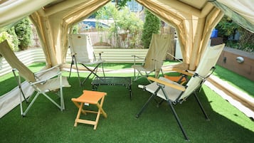 Een tent met vier canvasstoelen en een kleine tafel, omgeven door kunstgras.