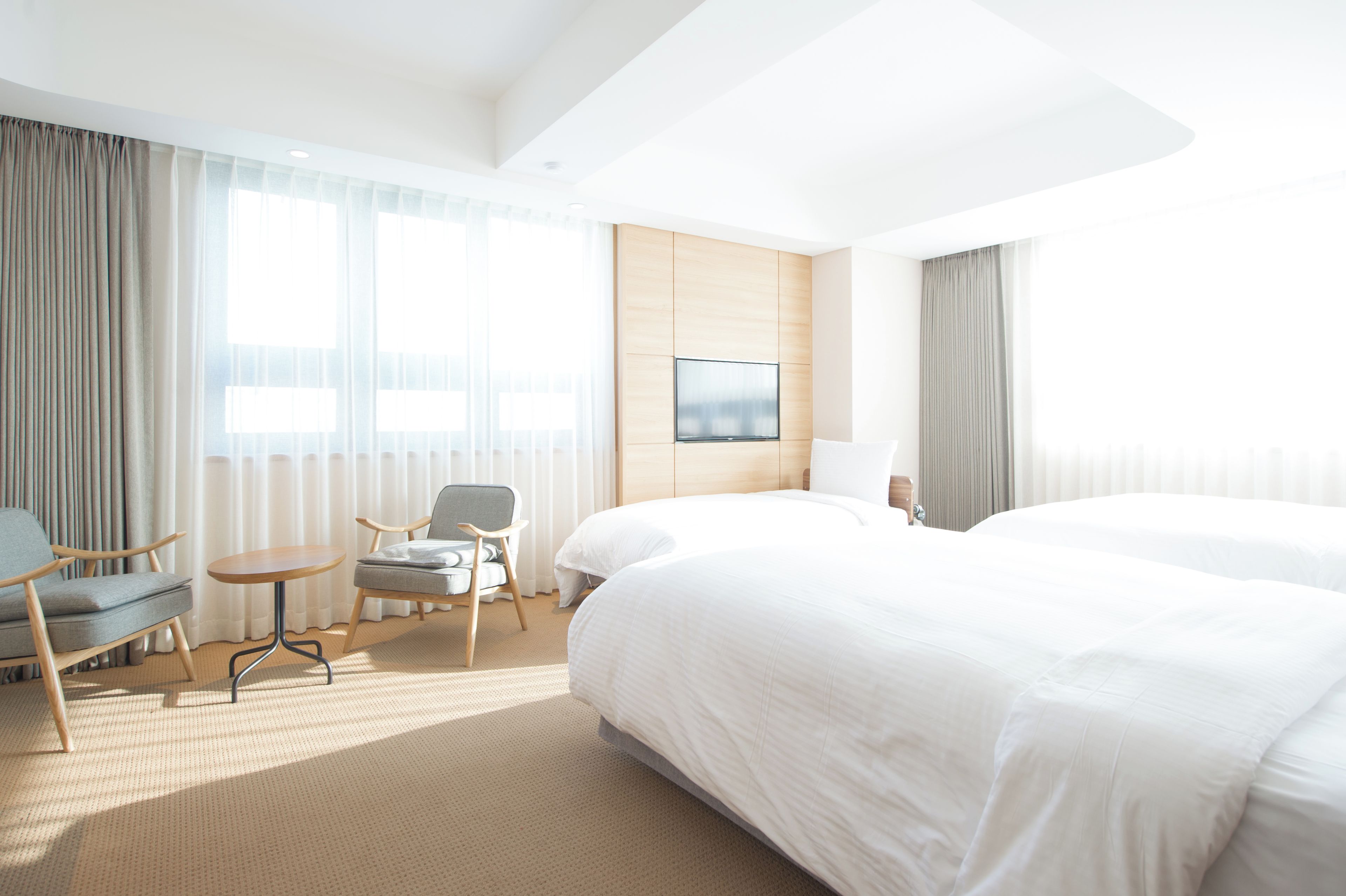 Ein Hotelzimmer mit einem großen Bett, zwei Sesseln, einem kleinen Tisch und einem Fernseher an der Wand.