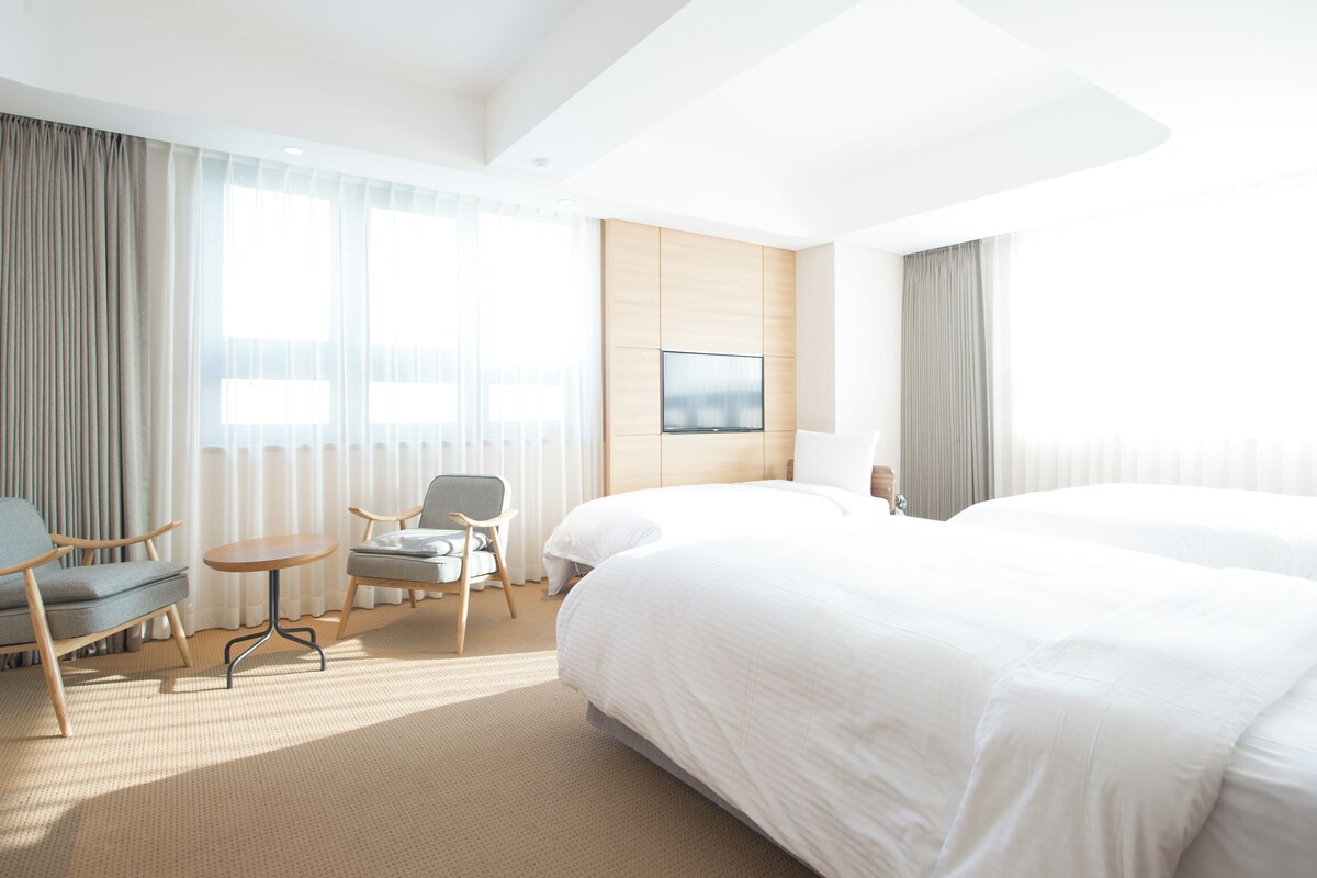 A hotel room with a large bed, two armchairs, a small table, and a TV on the wall.