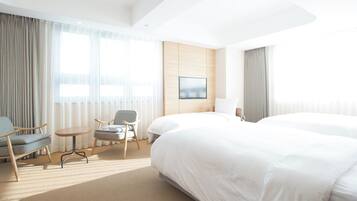 Ein Hotelzimmer mit einem großen Bett, zwei Sesseln, einem kleinen Tisch und einem Fernseher an der Wand.