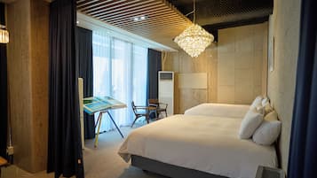 Habitación de hotel con una cama grande, un escritorio con silla, un ventilador de pie y un ventanal con cortinas.