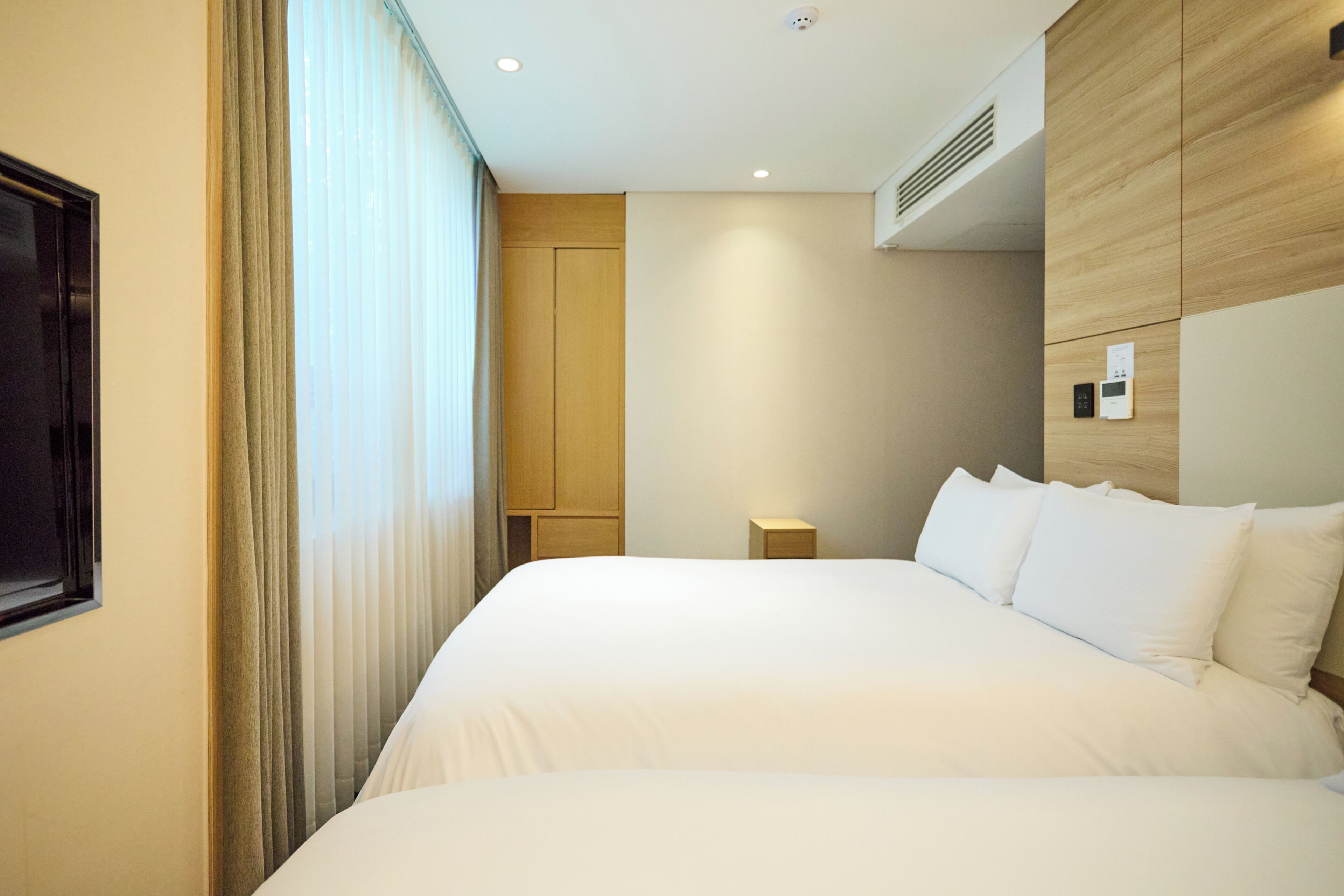 Habitació d'hotel amb un llit gran, una taula de nit, un panell de control fixat a la paret i una finestra amb cortines.