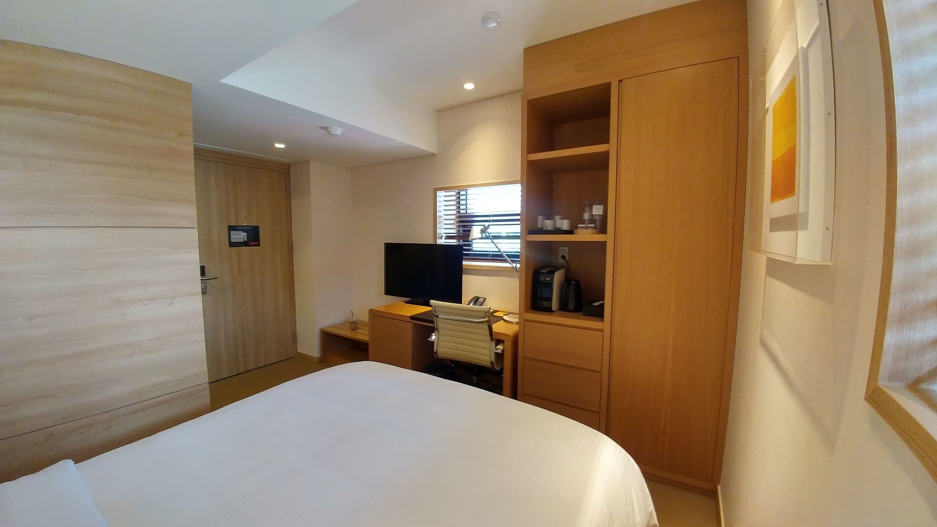 Ein Hotelzimmer mit einem Bett, einem Schreibtisch mit Computer, einem Fernseher und einem Kleiderschrank.
