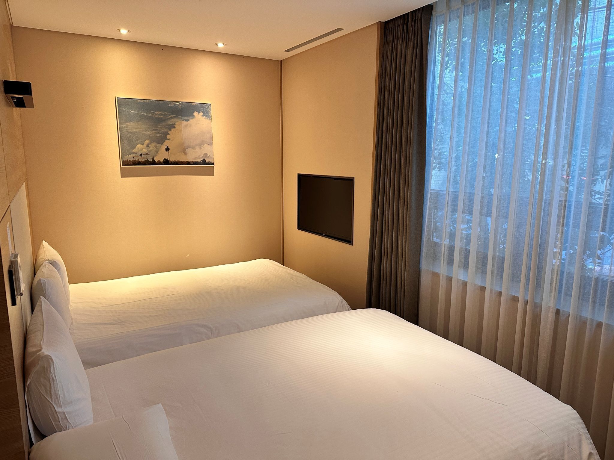 Habitación de hotel con dos camas, un cuadro en la pared, un televisor de pantalla plana y una ventana con cortinas.