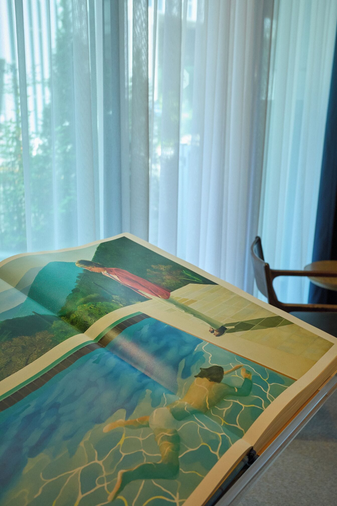 Una habitación con un ventanal grande, una mesa con una obra de arte colorida y una silla.
