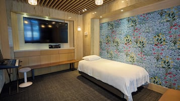 A bedroom with a bed, a desk with a keyboard, a TV, and a floral wallpaper.