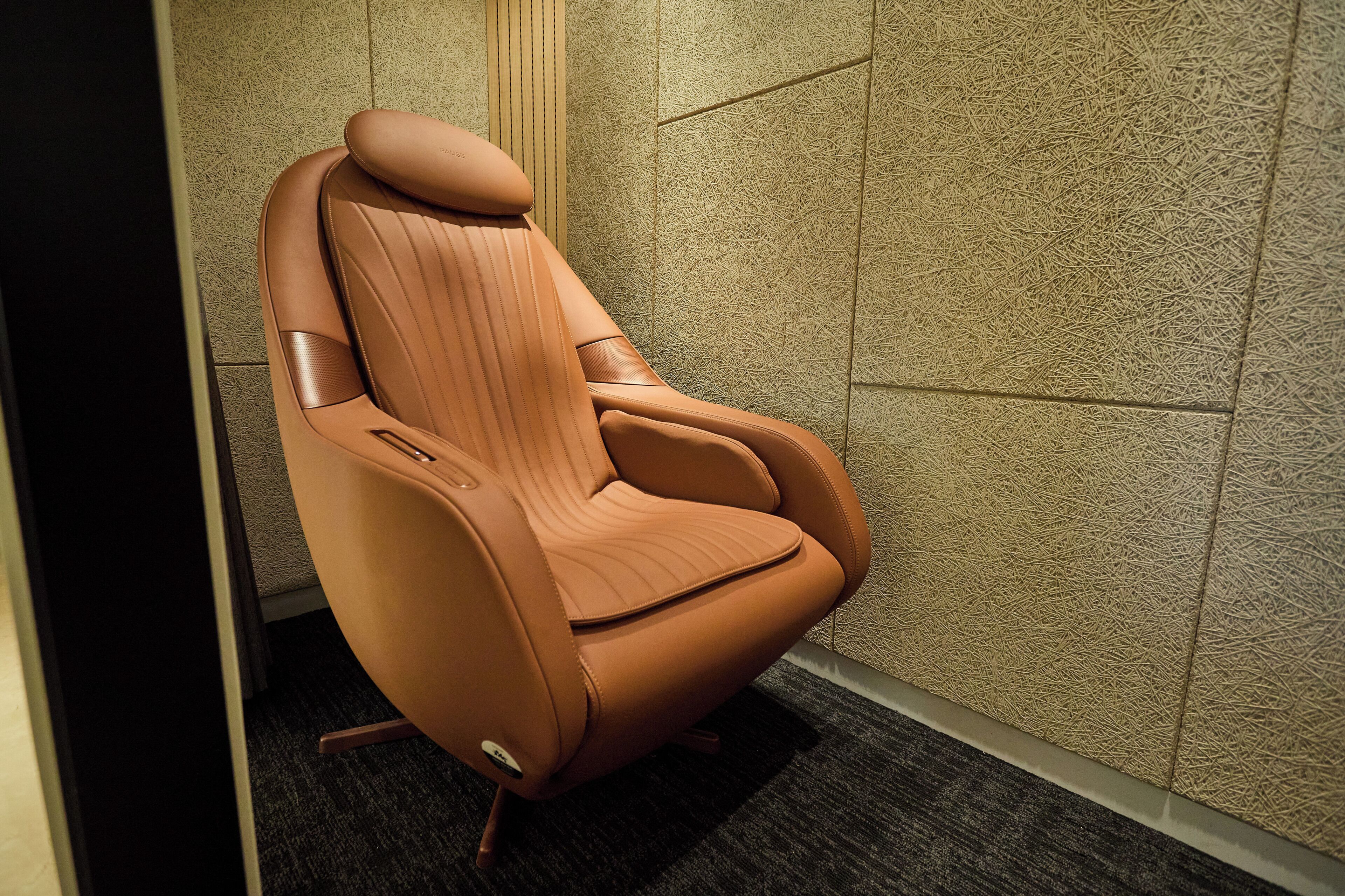 A modern, curved chair with a high backrest and armrests, positioned against a textured wall.