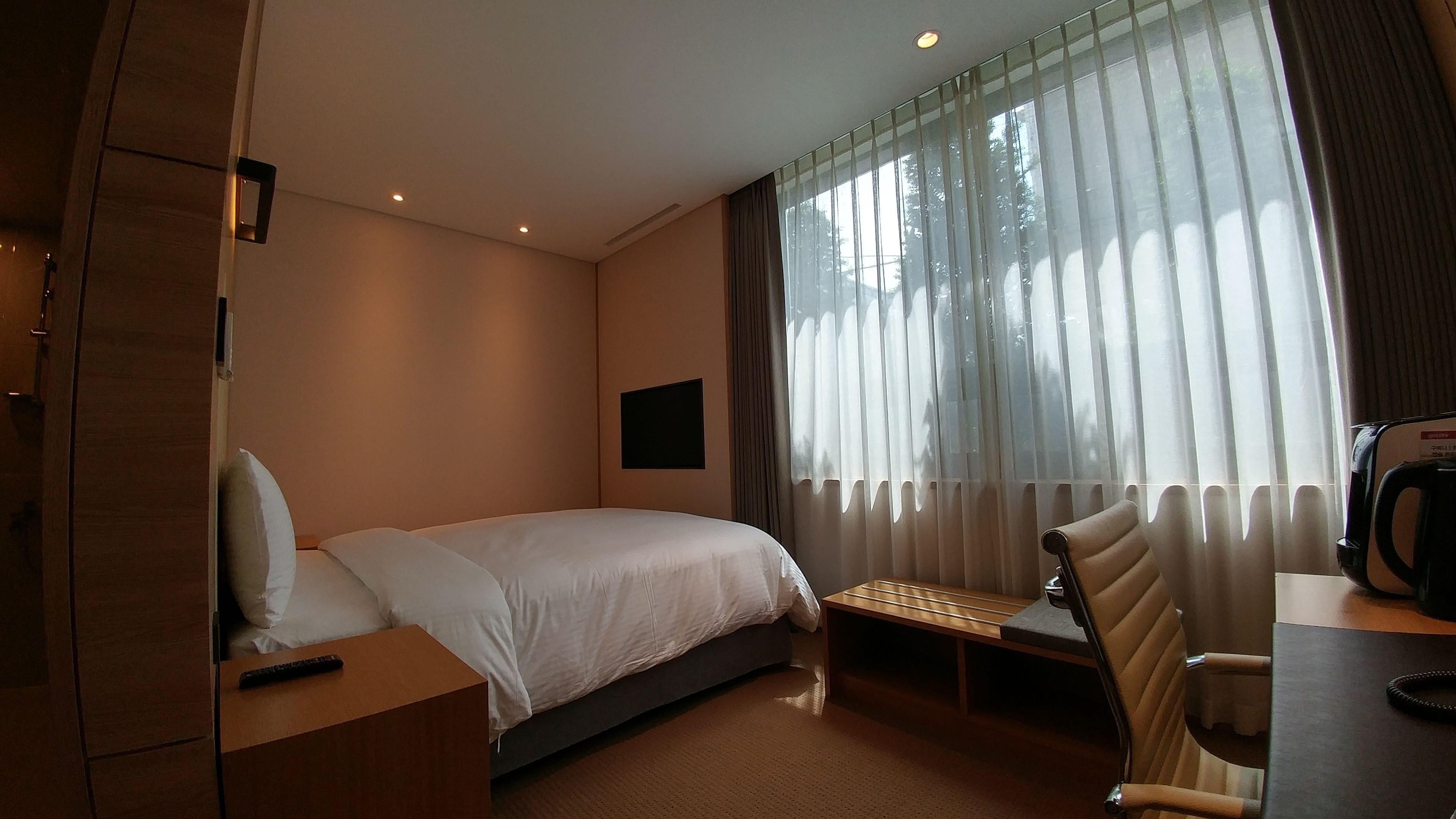 A hotel room with a bed, a desk with a chair, a television, and a window with curtains.