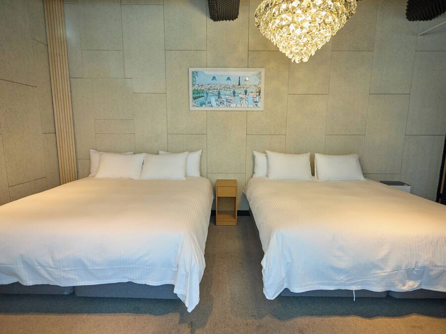 Habitación de hotel con dos camas, un cuadro de un paisaje urbano y una araña.