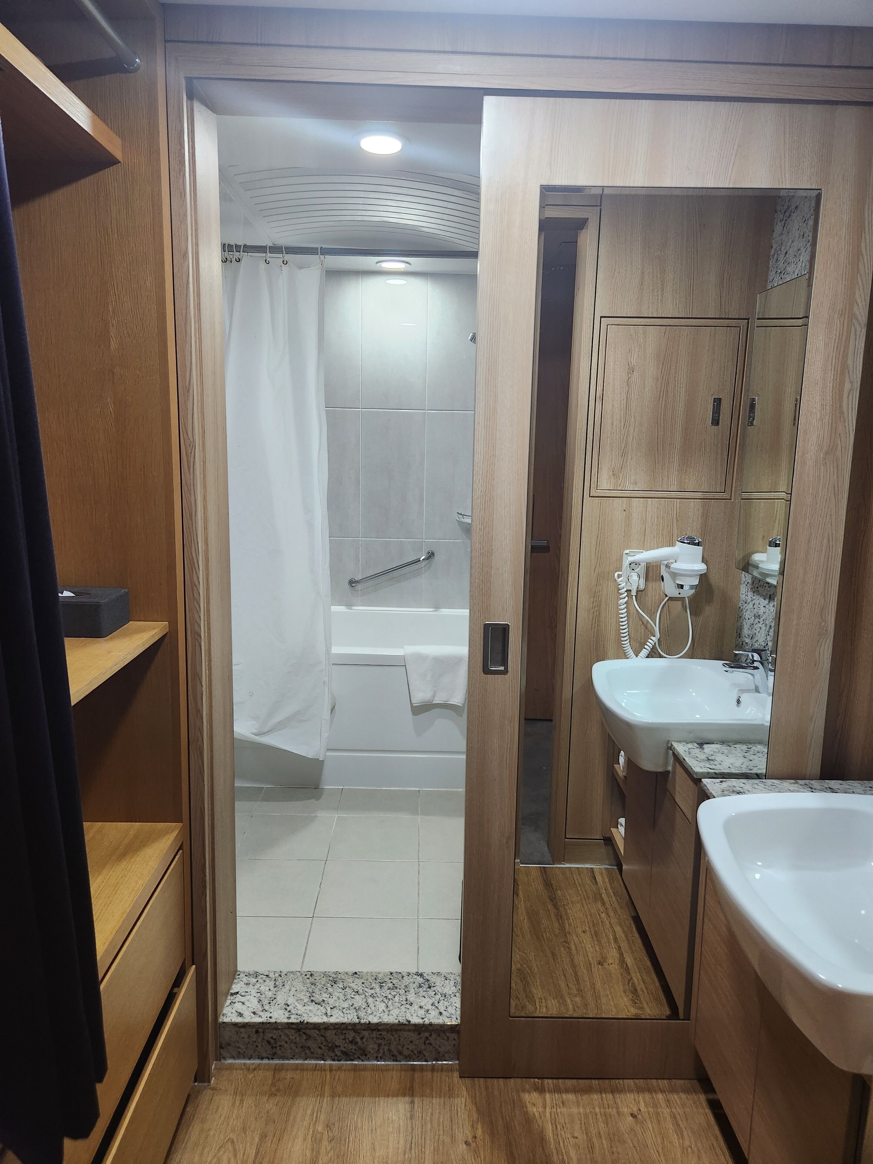 Un baño moderno con muebles de madera, ducha con cortina, bañera y lavamanos con espejo.