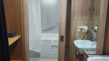 Un baño moderno con muebles de madera, ducha con cortina, bañera y lavamanos con espejo.
